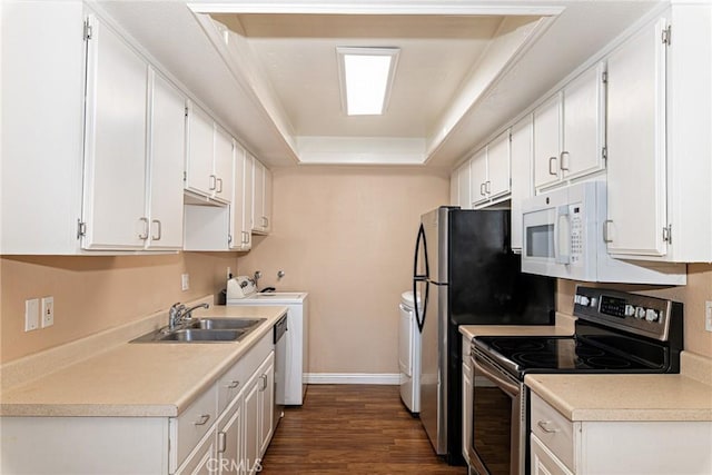 kitchen with dark wood-style flooring, a tray ceiling, stainless steel range with electric stovetop, washing machine and dryer, and a sink