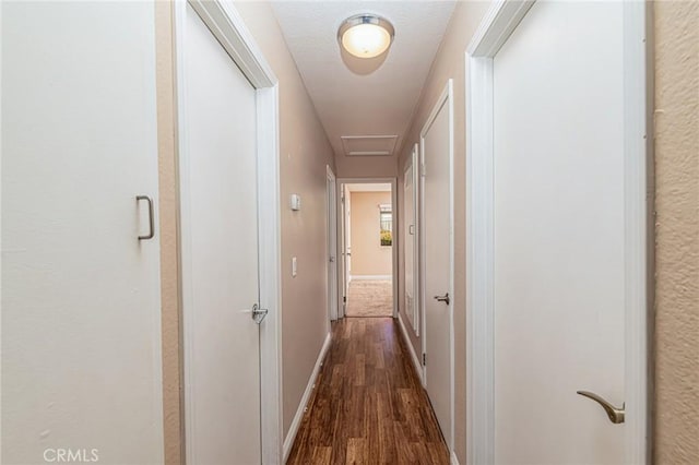 corridor featuring dark wood-style floors, attic access, and baseboards