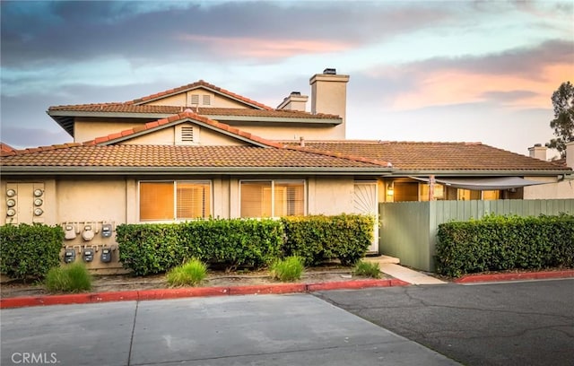 view of front of house with a tile roof, fence, a chimney, and stucco siding