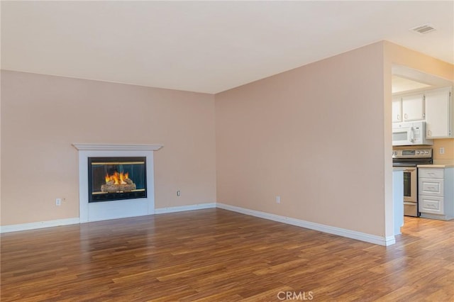 unfurnished living room with light wood-style floors, a glass covered fireplace, visible vents, and baseboards