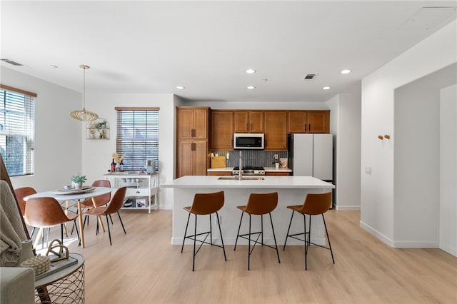 kitchen featuring tasteful backsplash, visible vents, light countertops, light wood-type flooring, and brown cabinetry