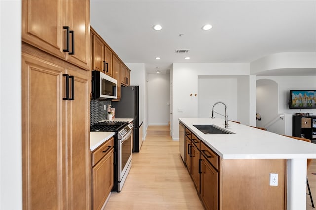 kitchen with a center island with sink, stainless steel appliances, visible vents, decorative backsplash, and a sink