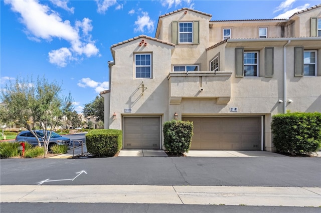townhome / multi-family property featuring an attached garage, a tiled roof, driveway, and stucco siding