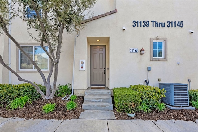 property entrance featuring central AC, a tiled roof, and stucco siding