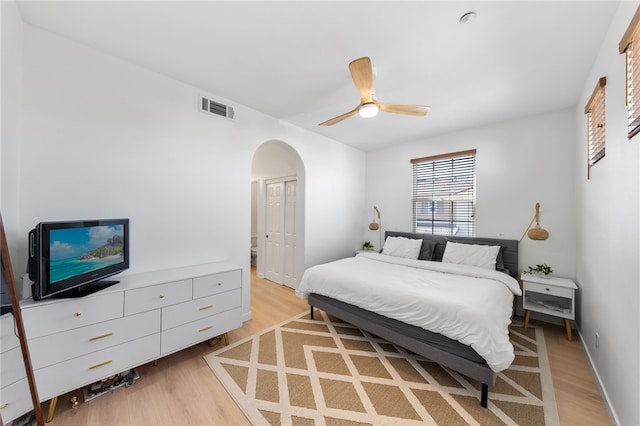 bedroom featuring visible vents, arched walkways, ceiling fan, light wood-type flooring, and a closet