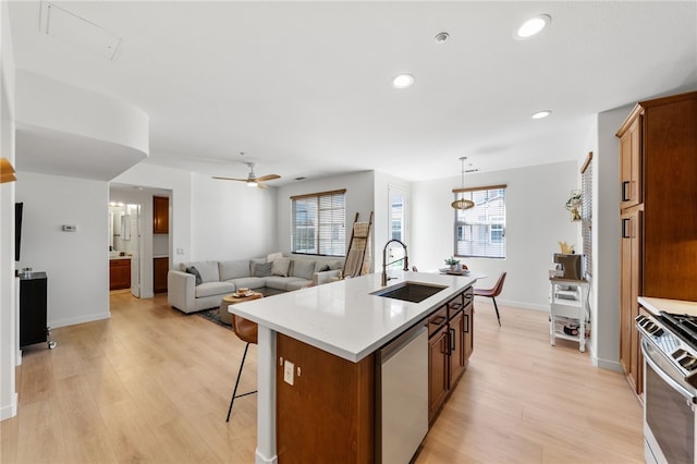 kitchen with a kitchen breakfast bar, a kitchen island with sink, appliances with stainless steel finishes, light wood finished floors, and a sink