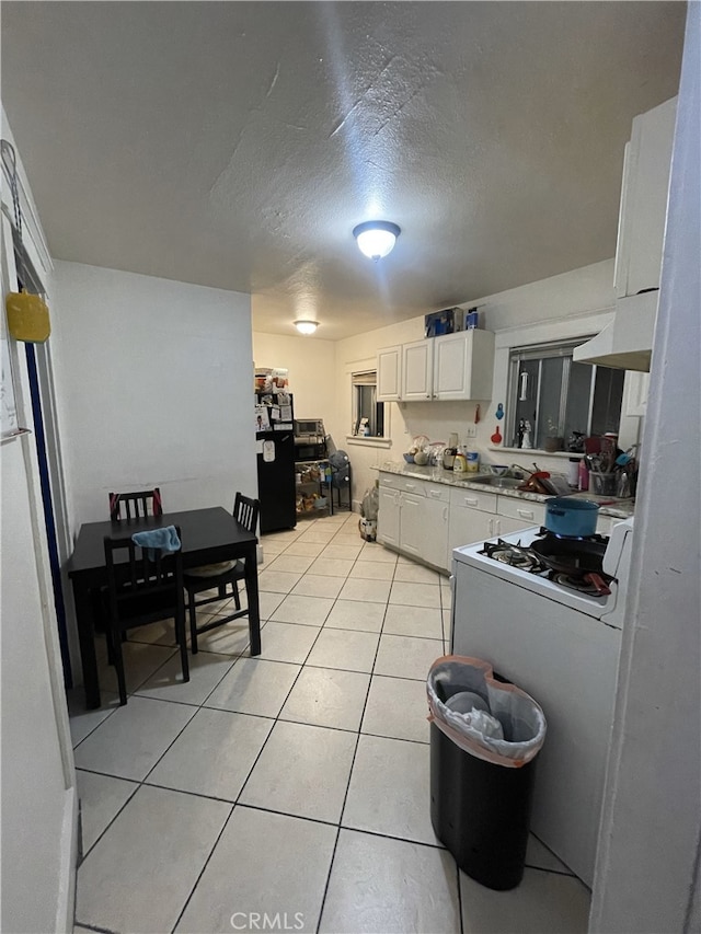 kitchen with light tile patterned floors, white cabinets, freestanding refrigerator, a textured ceiling, and under cabinet range hood