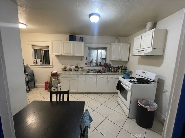 kitchen featuring white range with gas stovetop, white cabinetry, under cabinet range hood, and light tile patterned floors