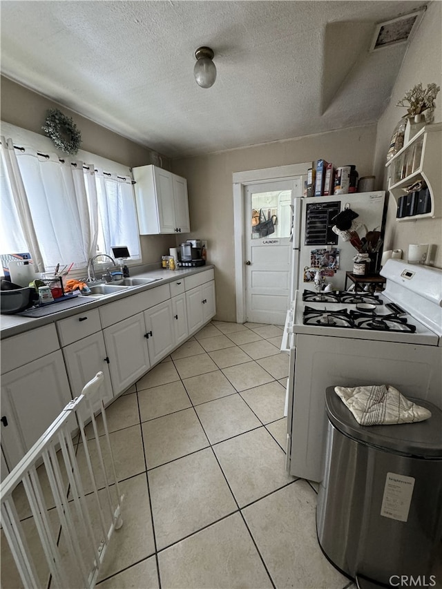 kitchen with light tile patterned floors, a textured ceiling, white cabinetry, white gas range oven, and freestanding refrigerator