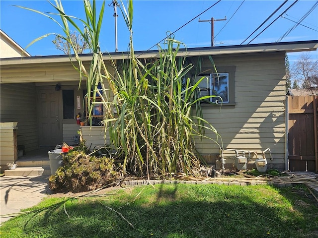 view of side of property with covered porch, a lawn, and fence