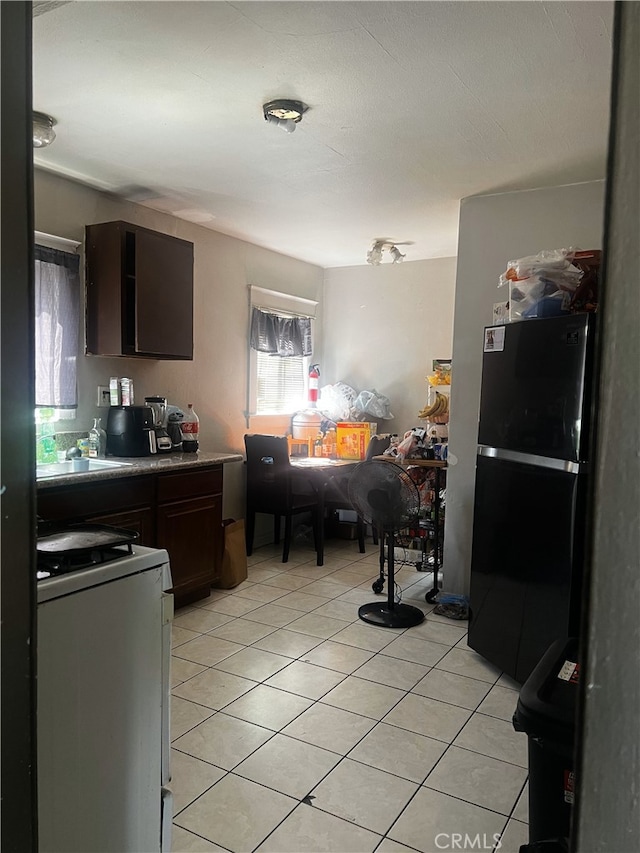 kitchen with light tile patterned flooring, stove, open floor plan, dark brown cabinets, and freestanding refrigerator