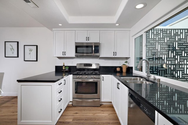 kitchen featuring a peninsula, wood finished floors, a sink, visible vents, and appliances with stainless steel finishes