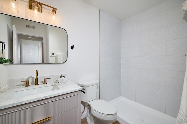 full bathroom featuring toilet, tiled shower, vanity, and visible vents