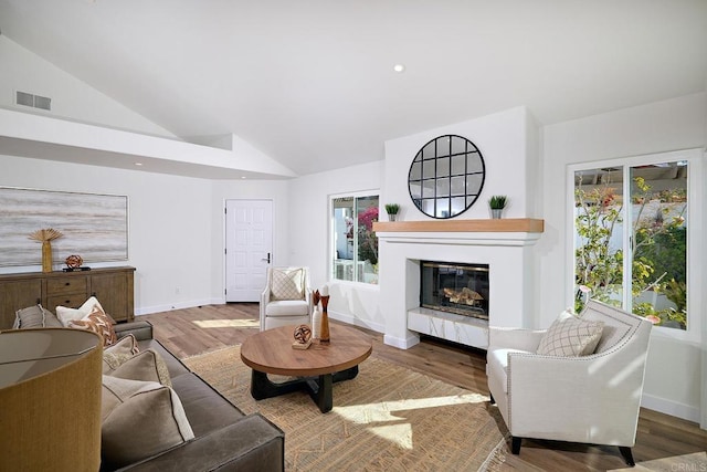 living room with recessed lighting, a glass covered fireplace, vaulted ceiling, wood finished floors, and baseboards