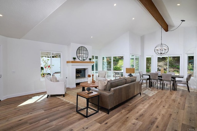 living area with light wood finished floors, a chandelier, a glass covered fireplace, high vaulted ceiling, and beam ceiling