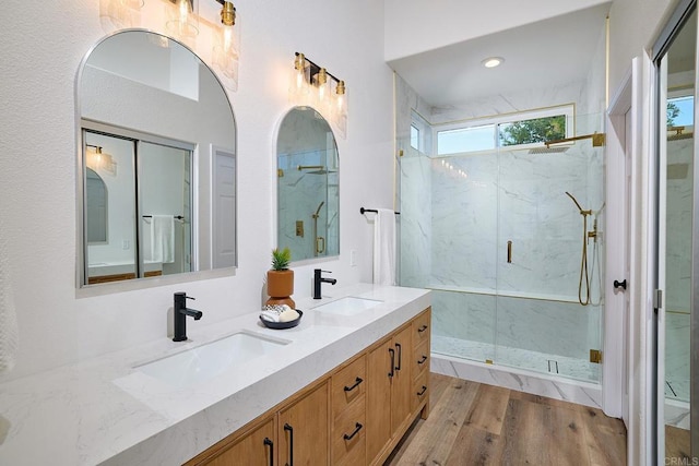 full bathroom with double vanity, wood finished floors, a sink, and a marble finish shower