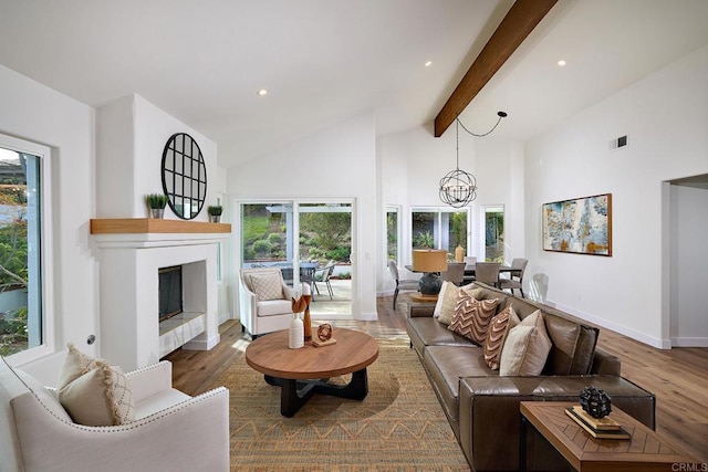 living area featuring beam ceiling, visible vents, a glass covered fireplace, wood finished floors, and high vaulted ceiling