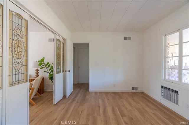 spare room with light wood-style floors, a wall mounted air conditioner, visible vents, and baseboards