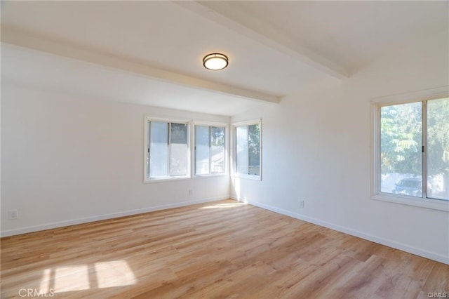 spare room featuring beamed ceiling, light wood-style flooring, and baseboards