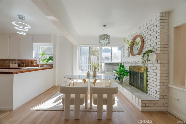 dining area with a chandelier, light wood-style flooring, a brick fireplace, and a wealth of natural light