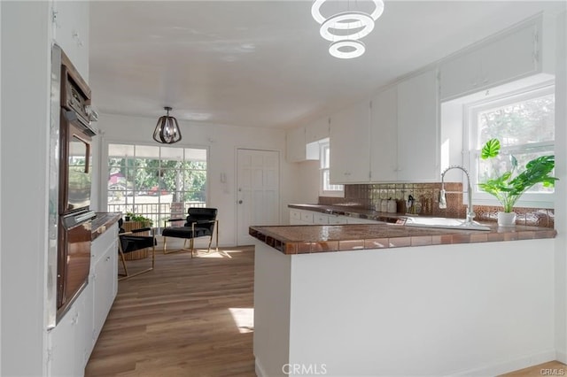 kitchen with tasteful backsplash, wood finished floors, a peninsula, white cabinetry, and a sink