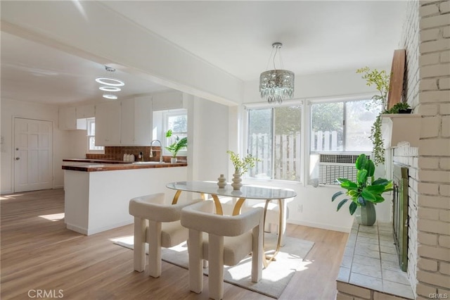 dining room featuring plenty of natural light, a fireplace, light wood-style flooring, and baseboards