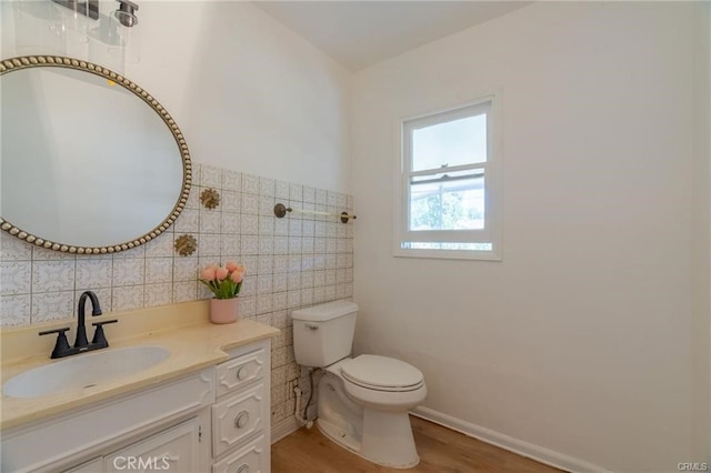 half bathroom with tile walls, toilet, vanity, wood finished floors, and baseboards