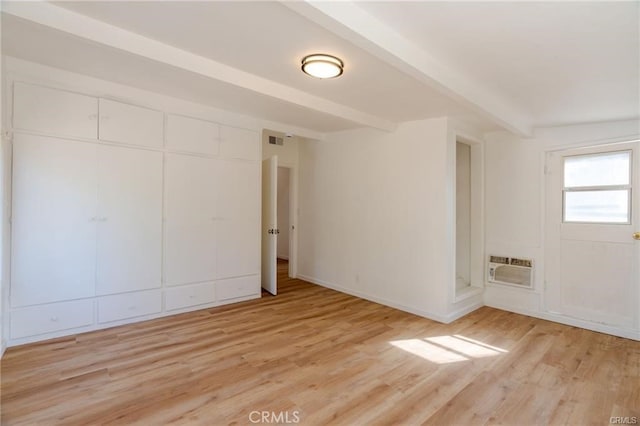 unfurnished room featuring light wood-style flooring, visible vents, baseboards, a wall mounted AC, and beam ceiling