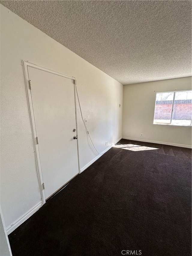 unfurnished room with baseboards, dark carpet, and a textured ceiling