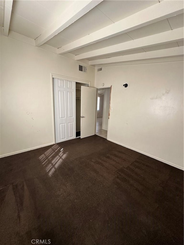 spare room with dark colored carpet, beamed ceiling, visible vents, and baseboards