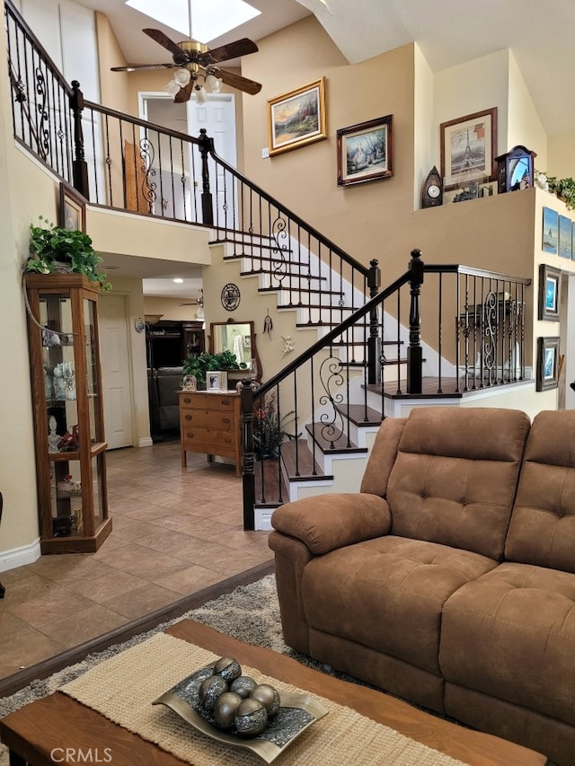 living room featuring ceiling fan, a high ceiling, stairway, and baseboards