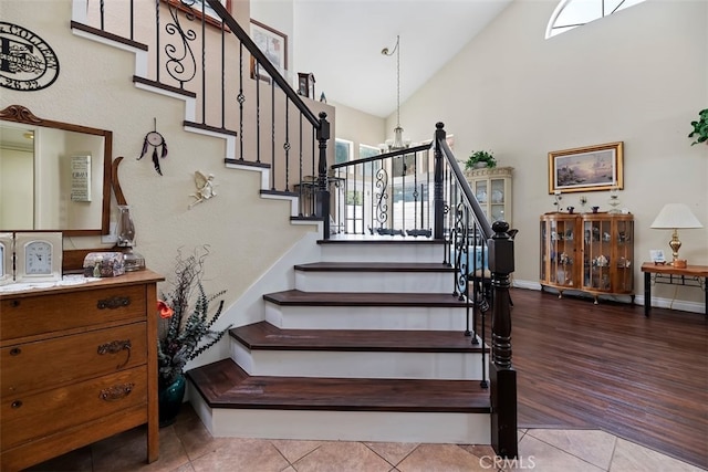 staircase featuring tile patterned floors, high vaulted ceiling, baseboards, and a chandelier