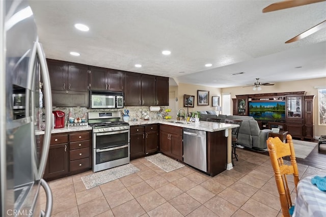 kitchen featuring a ceiling fan, appliances with stainless steel finishes, a peninsula, open floor plan, and dark brown cabinets