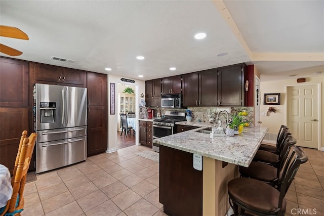 kitchen with a kitchen breakfast bar, stainless steel appliances, a sink, visible vents, and a peninsula