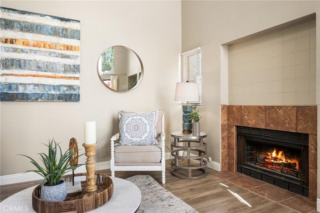 sitting room with a tiled fireplace, baseboards, and wood finished floors