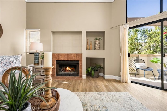 living area with baseboards, a tiled fireplace, a high ceiling, and wood finished floors