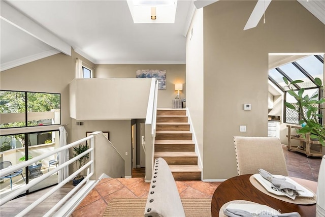 stairs with visible vents, a ceiling fan, ornamental molding, tile patterned floors, and lofted ceiling with skylight