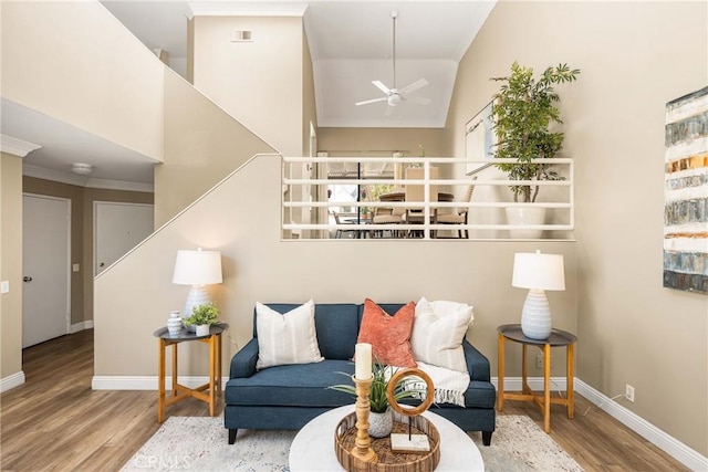 living room featuring ceiling fan, wood finished floors, a towering ceiling, baseboards, and ornamental molding