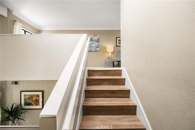 stairs featuring a textured wall, visible vents, crown molding, and baseboards