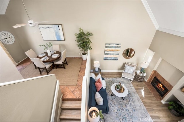 living area featuring ornamental molding, a glass covered fireplace, a ceiling fan, wood finished floors, and baseboards