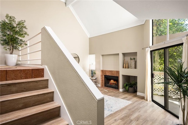 stairway with a fireplace, high vaulted ceiling, wood finished floors, and ornamental molding