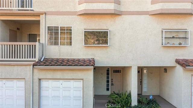 exterior space featuring a garage, a tile roof, a balcony, and stucco siding