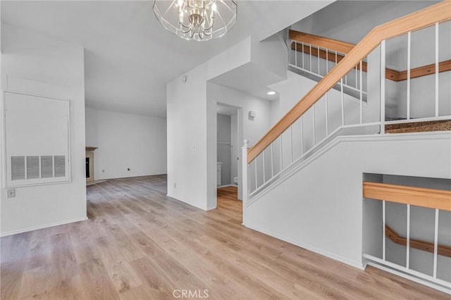 unfurnished living room featuring a notable chandelier, a fireplace, stairway, and wood finished floors