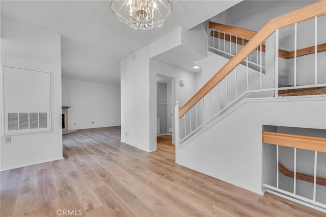 unfurnished living room with stairway, wood finished floors, baseboards, a fireplace, and a notable chandelier