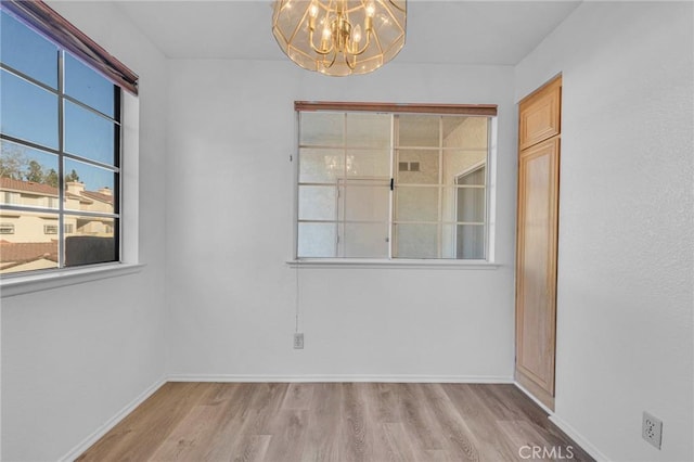 spare room featuring wood finished floors, baseboards, and an inviting chandelier
