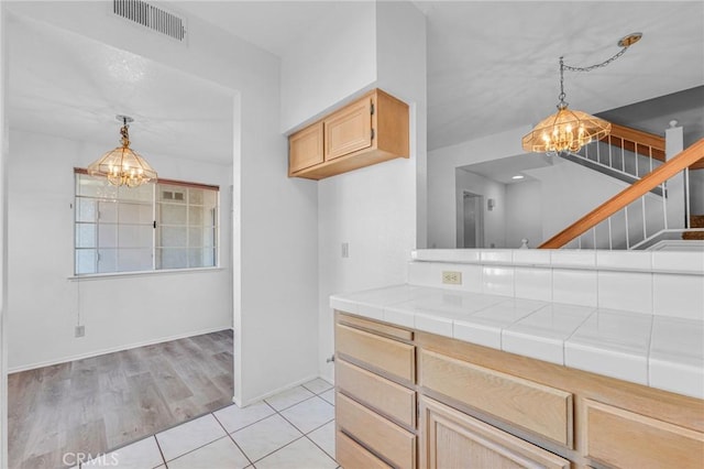 kitchen with tile countertops, hanging light fixtures, visible vents, and an inviting chandelier