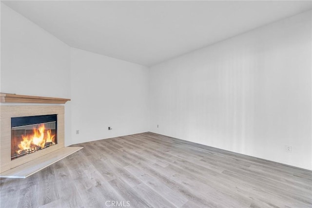 unfurnished living room featuring wood finished floors and a glass covered fireplace