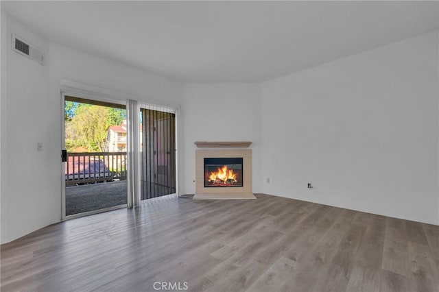 unfurnished living room with a warm lit fireplace, wood finished floors, and visible vents