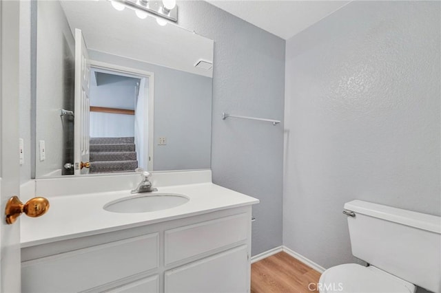 half bath with visible vents, baseboards, toilet, wood finished floors, and vanity