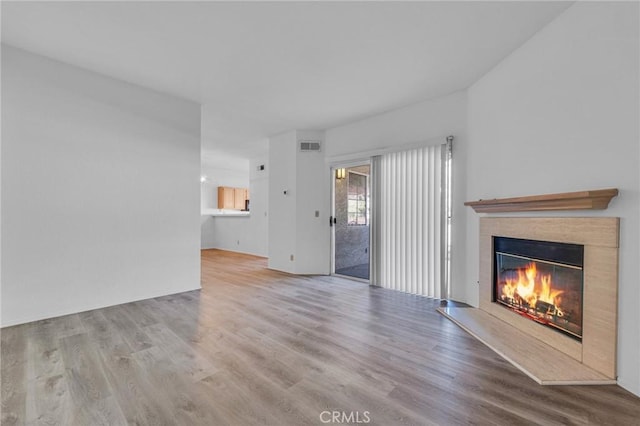 unfurnished living room featuring a glass covered fireplace, visible vents, and wood finished floors